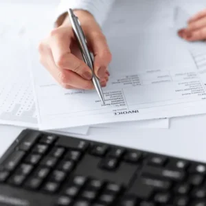 A person writing on paper next to a keyboard.